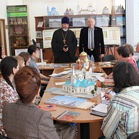 Участники семинара за столом в читальном зале ГБУК НОСБ. На столе выставка многоформатных изданий и макетов церквей