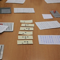 На фото: разложенные на столе приборы и грифели для письма по системе Брайля - крупным планом.