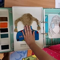 Воспитанница детского сада тактильно исследует разворот с изображением волос из книги «В гостях у парикмахера»