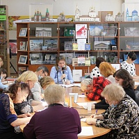 На фото: В читальном зале, за столом сидят читатели и пишут диктант. В центре, за столом сидит сотрудник НОСБ Л.Р. Бабешко диктующая текст.