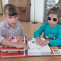 Ирина и Аймээрим (слева направо) тактильно исследуют книгу «У портного» из «Дома мастеров»